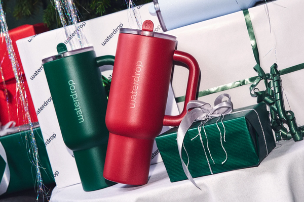 Rote und grüne isolierte Becher mit Griffen lehnen an einer weißen Oberfläche neben eingepackten Geschenken und silbernen Girlanden.